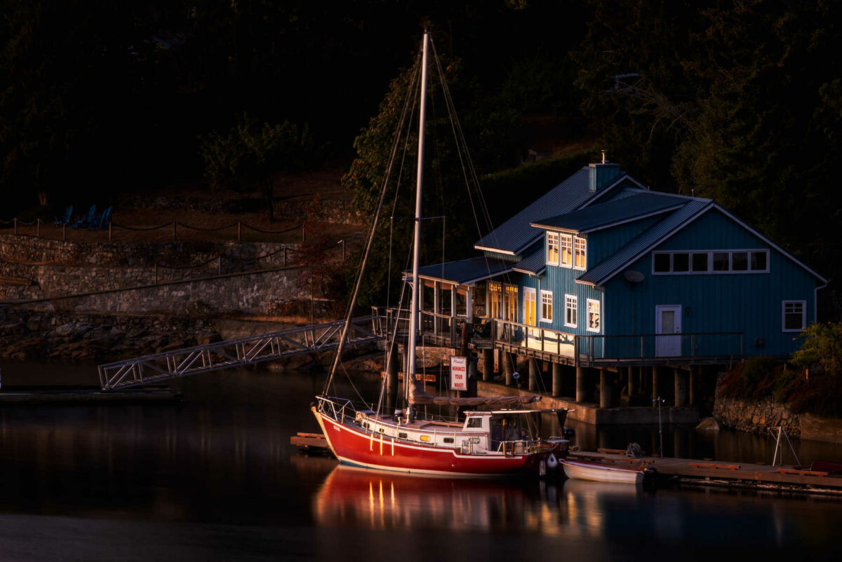 Perahu layar berwarna merah diparkir tepat di dekat rumah berwarna biru yang dibangun di tepi danau
