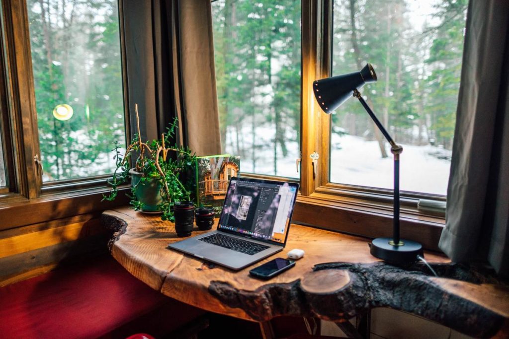 Een houten bureau met laptop en telefoon bij het raam