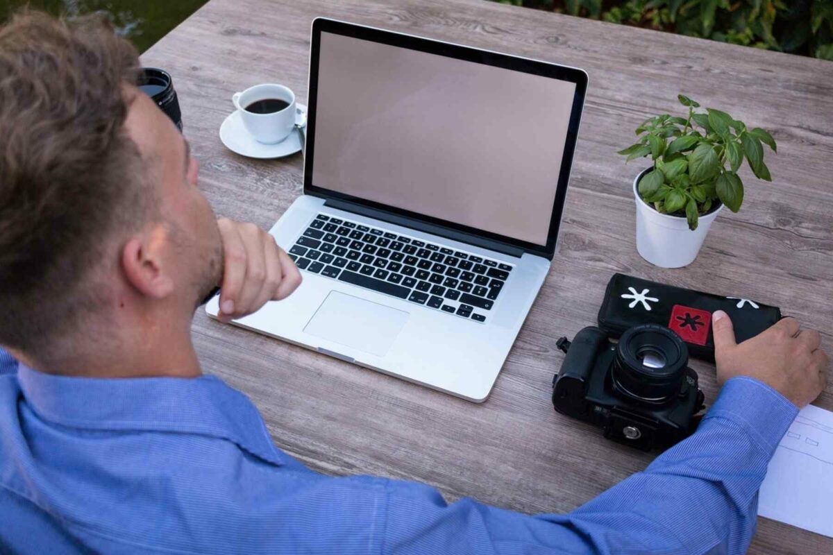 Un uomo guarda il suo laptop con accanto una fotocamera DSLR